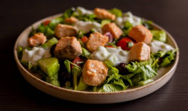 Lezzetli bir Akdeniz salatasına yakın plan. İçinde somon filetosu ve bir tutam tzatziki sosu var. Taze ve lezzetli bir yemek deneyimi sunuyor.