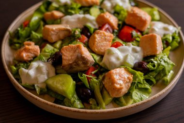 Lezzetli bir Akdeniz salatasına yakın plan. İçinde somon filetosu ve bir tutam tzatziki sosu var. Taze ve lezzetli bir yemek deneyimi sunuyor.