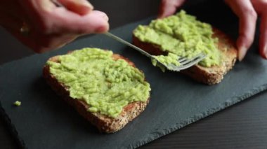 Bir dilim ekmeğin üzerine kremalı avokado döken birinin büyüleyici yakın çekim videosu bu besleyici atıştırmalığın basitliğini ve lezzetini vurguluyor.