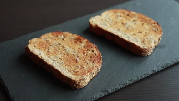 新鮮なトーストパンのスライスをダークストーンボードに置いたクローズアップストックビデオは その黄金の地殻を強調し テクスチャを誘う — ストック動画