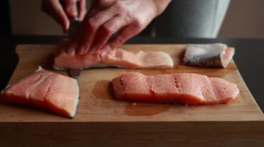 Ahşap bir tahtanın üzerindeki somon filetosunun derisini nazikçe yüzen bir kadının ellerini gösteren ve taze deniz ürünlerinin hazırlıklarını gösteren yakın plan bir video.