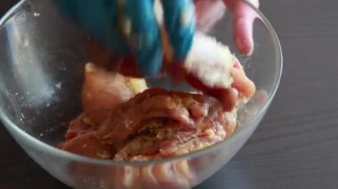 Kadın elleri, bu yakın çekim videosunda baharatı kemiksiz tavuk butlarına güzelce sürterek cam kaseye koyuyor.