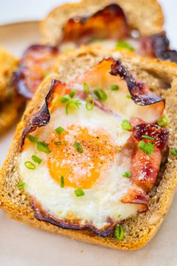 Beyaz tabakta pişmiş domuz pastırması ve yumurta ve taze yeşil soğan yakın plan