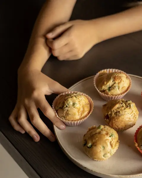 stock image Kid's Hand Reaching for a Savory Muffin with Pea and Ham from Plate Close-Up on Dark Background