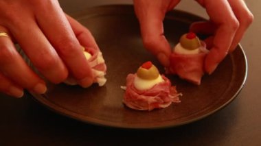 Kadınların elleri Cadılar Bayramı 'nda Prosciutto, Mozzarella ve Yeşil Zeytinli Korku Elleri Yemeği hazırlıyor.