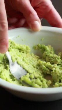 Olgun bir avokadoyu çatalla beyaz bir kasede ezmek.