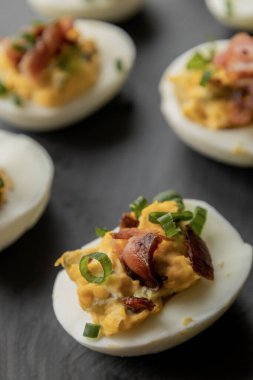  deviled eggs topped with crispy bacon and green onion, creating a savory and colorful appetizer. Perfect for party starters, gatherings, or holiday platters clipart