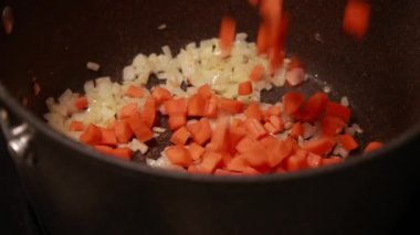 Koyu bir kapta sotelenmiş soğan ve havuç yakın plan.