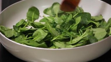 Beyaz bir tavada pişirilen taze ıspanağın yakın plan çekimi. Tahta bir kaşıkla karıştırılmış.