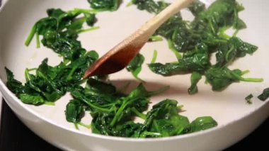 Beyaz bir tavada pişirilen taze ıspanağın yakın plan çekimi. Tahta bir kaşıkla karıştırılmış.