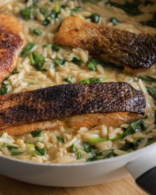 Pişmiş somon filetosu, beyaz bir tavada makarna ve ıspanak, sağlıklı ve lezzetli bir yemek sergiliyor.