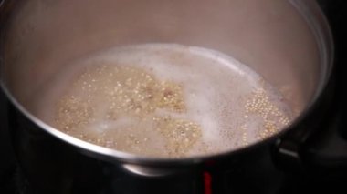 Küçük bir tencerede kinoa pişirirken yakın çekim, tahılların kaynaması ve suyu emmesi, sağlıklı ve besleyici bir yemek için mükemmel.