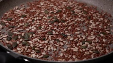 Bir tavada pişirilen ayçiçeği, balkabağı ve keten tohumlarının karışımının yakın çekim videosu sağlıklı ve besleyici bir bileşen hazırlıyor.