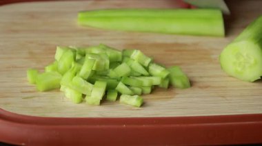 Kadın elleri ahşap kesim tahtasının üzerinde salatalık doğruyor.