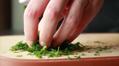 Kadın elleri ahşap kesme tahtasının üzerinde taze dereotu kesiyor.