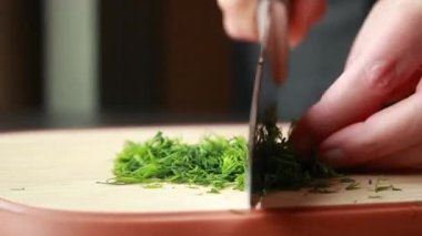 Kadın elleri ahşap kesme tahtasının üzerinde taze dereotu kesiyor.