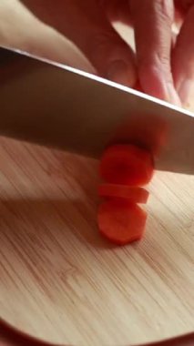  woman hands slicing carrot on wooden board close-up