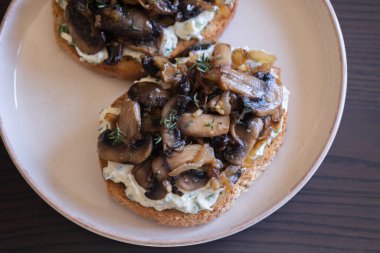 Lezzetli mantarlı tost, krem peynirli, mantarlı ve karamelli soğanlı, yakın plan beyaz tabakta.