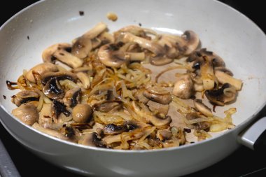 Beyaz bir tavada mantar ve soğan pişirmek.