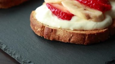Lezzetli kızarmış ekmek, çırpılmış ricotta, muz ve yakın plan çilek dilimleri.