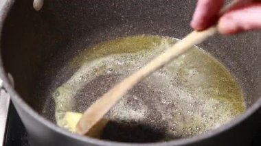  Zeytinyağı ve tereyağı yakın çekim bir tencerede birlikte ısıtılıyor. Malzemeler erimeye başlar, bu da yemek pişirmek için zengin bir temel oluşturur.