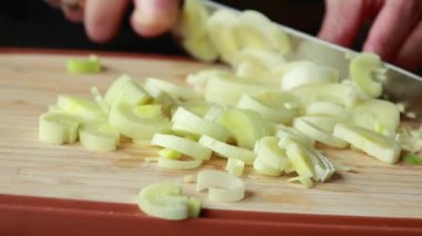 Kadının elleri, tahta kesme tahtasındaki pırasayı dikkatlice kesiyor.