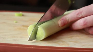 Kadının elleri, tahta kesme tahtasındaki pırasayı dikkatlice kesiyor.