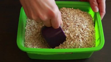 Yulafları bardakla ölçen bir kadın elinin yakın çekimi. Yulaflar dikkatlice kepçelenir ve sağlıklı bir kahvaltı veya pişirme için kullanılmaya hazırdır..