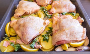  Çiğ tavuk budu, patates, limon ve soğan tablasında yakın plan pişirmeye hazır.