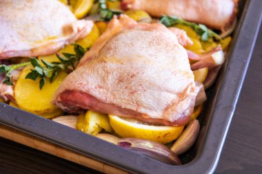  Çiğ tavuk budu, patates, limon ve soğan tablasında yakın plan pişirmeye hazır.