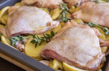  Çiğ tavuk budu, patates, limon ve soğan tablasında yakın plan pişirmeye hazır.