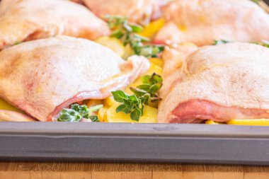  Çiğ tavuk budu, patates, limon ve soğan tablasında yakın plan pişirmeye hazır.