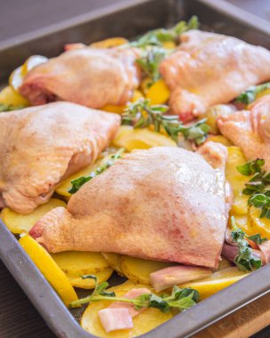  Çiğ tavuk budu, patates, limon ve soğan tablasında yakın plan pişirmeye hazır.