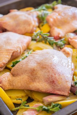  Çiğ tavuk budu, patates, limon ve soğan tablasında yakın plan pişirmeye hazır.