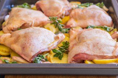  Çiğ tavuk budu, patates, limon ve soğan tablasında yakın plan pişirmeye hazır.