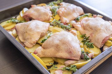  Çiğ tavuk budu, patates, limon ve soğan tablasında yakın plan pişirmeye hazır.