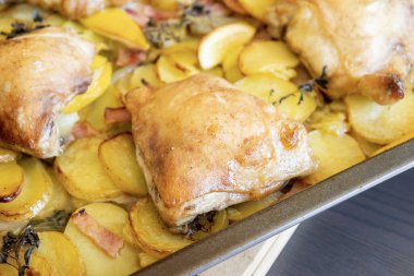 Patates, limon ve soğanlı kızarmış tavuk budu yakın plan bir tepside.