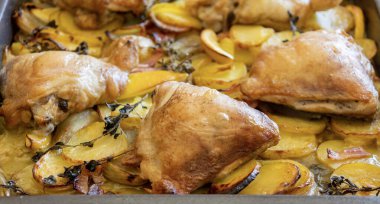 Patates, limon ve soğanlı kızarmış tavuk budu yakın plan bir tepside.