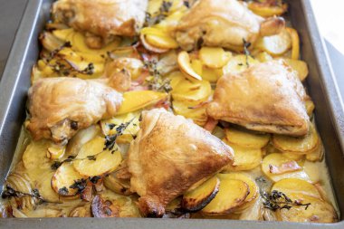 Patates, limon ve soğanlı kızarmış tavuk budu yakın plan bir tepside.