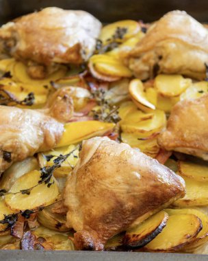 Patates, limon ve soğanlı kızarmış tavuk budu yakın plan bir tepside.