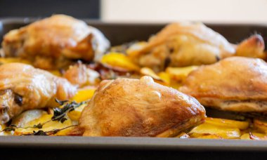 Patates, limon ve soğanlı kızarmış tavuk budu yakın plan bir tepside.