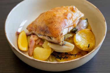 Kızarmış tavuk budu, patates, limon ve soğan ile yakın plan bir tabakta.