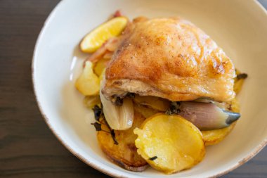 Kızarmış tavuk budu, patates, limon ve soğan ile yakın plan bir tabakta.