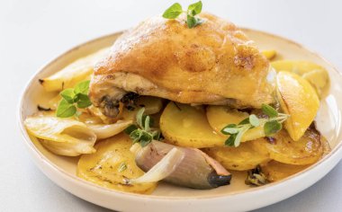 Kızarmış tavuk budu, patates, limon ve soğan ile yakın plan bir tabakta.