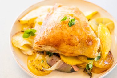 Kızarmış tavuk budu, patates, limon ve soğan ile yakın plan bir tabakta.