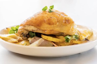 Kızarmış tavuk budu, patates, limon ve soğan ile yakın plan bir tabakta.