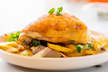 Kızarmış tavuk budu, patates, limon ve soğan ile yakın plan bir tabakta.