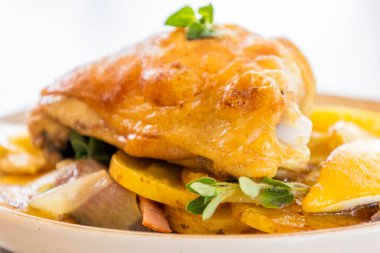 Kızarmış tavuk budu, patates, limon ve soğan ile yakın plan bir tabakta.