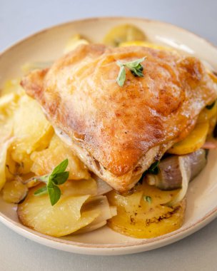 Kızarmış tavuk budu, patates, limon ve soğan ile yakın plan bir tabakta.