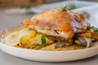 Kızarmış tavuk budu, patates, limon ve soğan ile yakın plan bir tabakta.